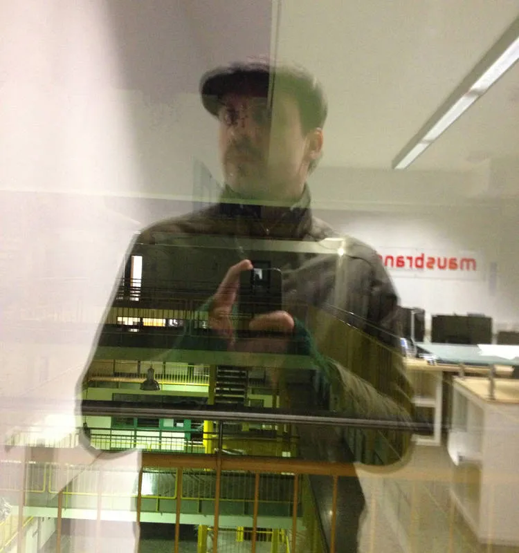 2013 — Portrait-Spiegelung in der Glastür des Mausbrand-Büros in Schwerte, Schiebermütze, grüne Handstulpen